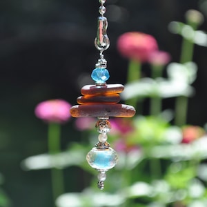 May include: A silver charm with a stack of brown sea glass and a blue crystal bead. The charm is hanging from a silver chain and has a blue crystal bead at the bottom.