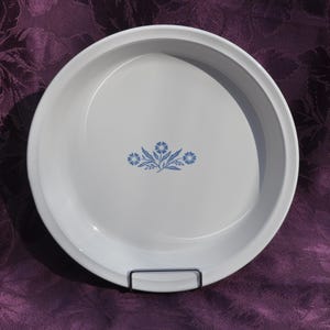 May include: White, round serving dish with a raised rim. The dish features a blue floral design in the center. The dish is sitting on a metal stand. A classic piece for serving food.