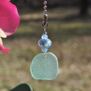 May include: A light blue sea glass pendant with a silver chain and a blue and white patterned bead.