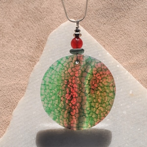 May include: A round green and red agate pendant with a silver chain and red bead. The pendant has a unique, natural pattern.