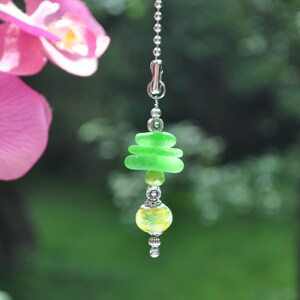 May include: A green glass bead light pull with a yellow and white floral bead and silver accents.