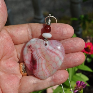 May include: A heart-shaped pendant made of pink and white agate with red and white beads on a silver chain.