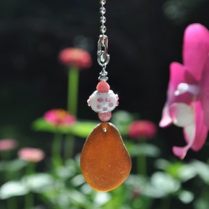 May include: A brown glass sea glass pendant with a white and pink beaded charm hanging from a silver chain.