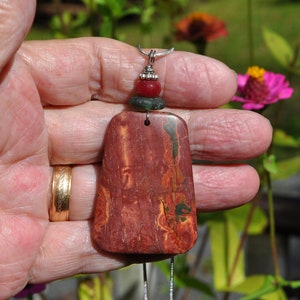 May include: A red, green, and silver pendant necklace with a large, rectangular, red and green stone. The stone has a marbled pattern.