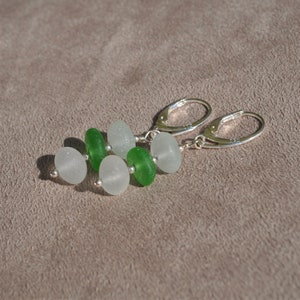 Puede incluir: Pendientes de plata con cierre de palanca y cuentas de vidrio marino esmerilado en blanco y verde. Los pendientes tienen un cierre de palanca. Las cuentas de vidrio marino de forma ovalada están ensartadas con pequeñas cuentas de plata.