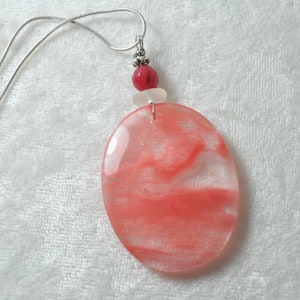 May include: A silver chain necklace with a pink and white oval pendant and a pink bead. The pendant has a swirling pattern.