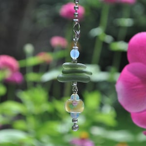 May include: A light blue glass bead hangs from a silver chain with a stack of three green glass beads and a yellow glass bead with a floral design.