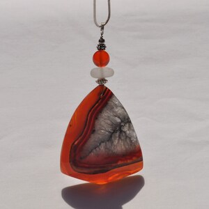 May include: A silver chain necklace with a triangular agate pendant featuring orange and white banding. The pendant is accented with a small silver bead and two carnelian beads.
