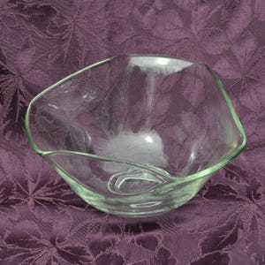 May include: A clear glass bowl with a unique, asymmetrical shape. The bowl has a slightly curved rim and a smooth, transparent surface. The bowl is designed for serving food or as a decorative piece.