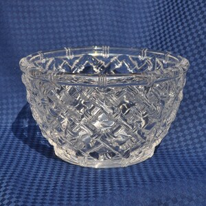 May include: A clear glass bowl featuring a raised, textured lattice pattern that mimics the appearance of woven bamboo stalks. The bowl has a circular rim and a rounded body, with the glass design creating a repeating crisscross motif.