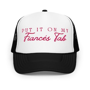 以下が含まれることがあります： ピンク色の「PUT IT ON MY Frances's Tab」の文字が入った、白と黒のトラッカーハット。白いフロントパネル、黒のメッシュバック、黒のつば、上部に黒いボタンが付いています。