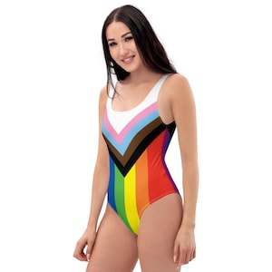 May include: A one-piece swimsuit with a rainbow and chevron pattern. The swimsuit is white with a pink, blue, brown, and black chevron pattern at the top. The bottom of the swimsuit is a rainbow pattern.
