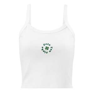 Puede incluir: Camiseta sin mangas blanca con tirantes finos. La parte superior presenta un trébol verde y las palabras "Zeta Alpha Tau" en un diseño circular. La parte superior está hecha de un material suave y cómodo.