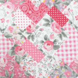 May include: A patchwork quilt featuring a repeating diagonal pattern of fabric squares. The design includes alternating blocks of pink and white gingham, white fabric with pink polka dots, and white fabric with a floral print of pink roses.