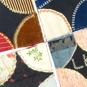 May include: A patchwork textile featuring four square sections, each composed of quarter-circle shapes in various fabrics. Colors include red stripes, black, brown velvet, and floral prints, with decorative stitching.