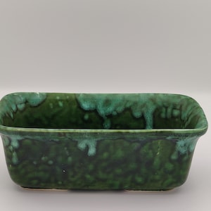 May include: A rectangular green ceramic planter with a mottled glaze. The planter has a slightly rounded bottom and a wide, shallow opening.