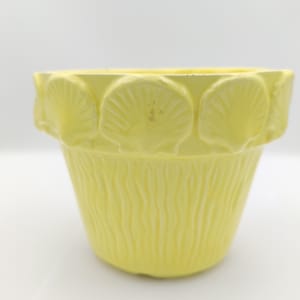 Könnte beinhalten: Ein gelber Keramiktopf mit einem gewellten Rand und einem strukturierten, wellenförmigen Design. Der Topf ist mit erhabenen Muschelformen verziert.