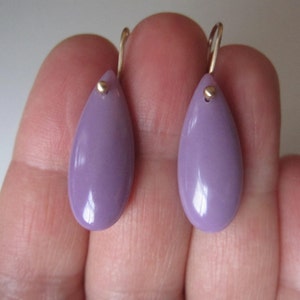 May include: A pair of teardrop-shaped earrings with a light purple color. The earrings are made of metal and have a gold-colored hook.