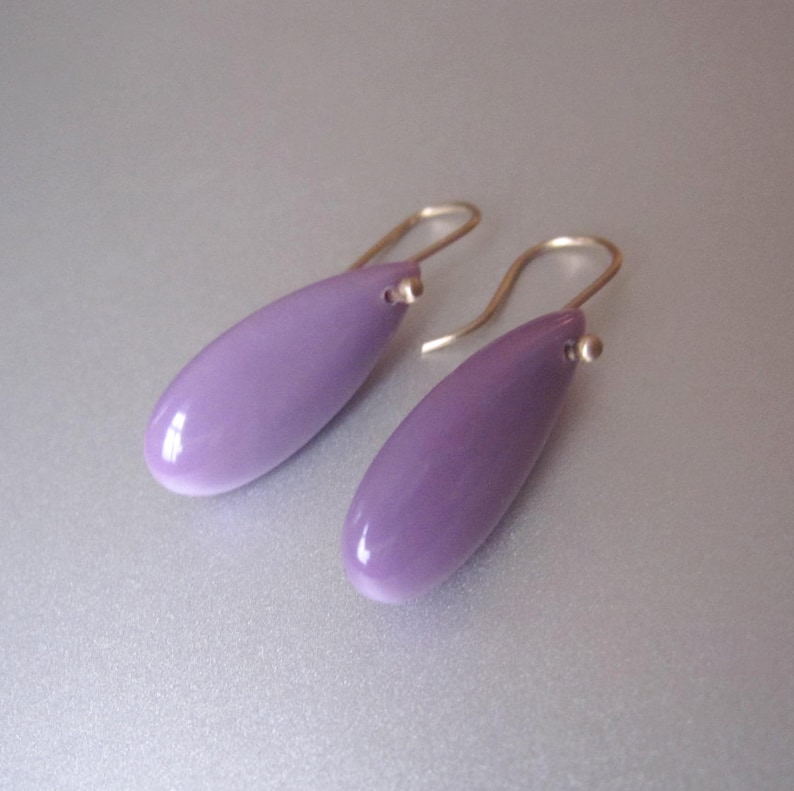 May include: A pair of purple teardrop-shaped earrings with gold hooks.