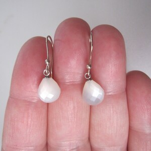 Op de afbeelding: Een paar zilveren oorhangers met witte, iriserende edelsteen druppels.