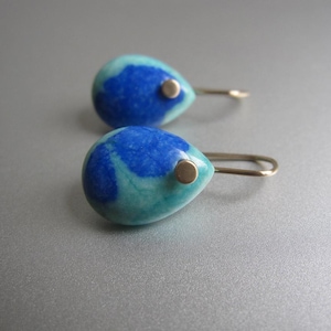 May include: A pair of teardrop-shaped earrings featuring a marbled pattern of deep royal blue and bright turquoise stone. Each earring is accented with a small, circular silver-toned metal stud at the top and includes a simple silver-toned hook wire.