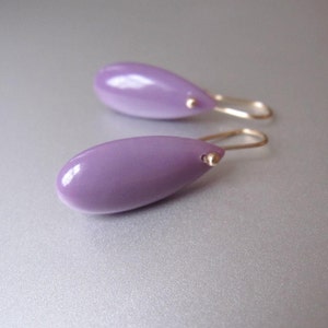 May include: A pair of dangle earrings with a light purple teardrop-shaped stone and a gold hook.