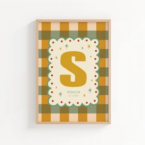 Puede incluir: Un estampado enmarcado con la letra "S" de color amarillo mostaza sobre un fondo crema, con un borde festoneado. El fondo es un patr&oacute;n de cuadros en tonos amarillos, verdes y crema. El nombre "Spencer" y una fecha est&aacute;n impresos debajo.
