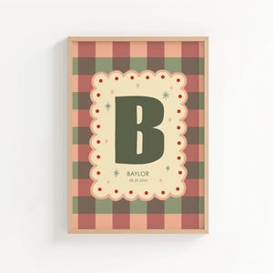 Puede incluir: Un estampado enmarcado con una gran letra "B" verde sobre un fondo crema festoneado. El fondo es un patr&oacute;n de cuadros en tonos rojos, verdes y beige. El nombre "Baylor" y la fecha est&aacute;n impresos debajo.