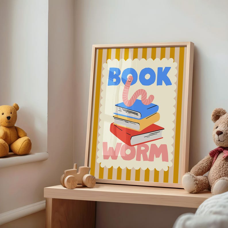 May include: A framed print featuring a stack of books with a smiling worm illustration. The words "BOOK WORM" are displayed in blue and pink. The print has a light wood frame and is set against a yellow and white striped background.
