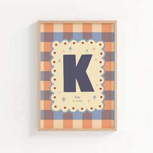 Puede incluir: Un estampado enmarcado con la letra "K" azul marino sobre un borde festoneado color crema. El borde est&aacute; decorado con peque&ntilde;os puntos rojos y estrellas. El fondo es un patr&oacute;n de cuadros naranja y azul. El texto "KAI 07.14.2024" est&aacute; en la parte inferior.