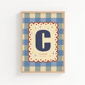 Puede incluir: Cuadro enmarcado con un fondo a cuadros azul y beige. Un dise&ntilde;o central con bordes festoneados muestra la letra "C" azul marino, el nombre "Connor" y la fecha "04.11.2021". El marco es de color madera clara.