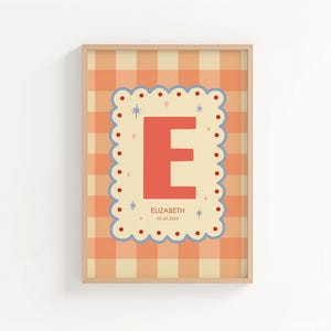 Puede incluir: Arte de pared enmarcado con una gran letra "E" coral sobre un fondo crema con un borde festoneado. El fondo tiene un patr&oacute;n de cuadros vichy melocot&oacute;n y crema. El nombre "ELIZABETH" y la fecha "08.20.2023" est&aacute;n impresos debajo de la letra.
