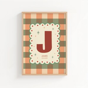 Puede incluir: Un estampado enmarcado con una gran letra "J" de color &oacute;xido sobre un fondo crema festoneado con puntos rojos y acentos de estrellas. El fondo es un patr&oacute;n de cuadros en naranja, verde y crema. El nombre "JAMES" y la fecha "03.20.2023" est&aacute;n debajo.