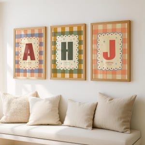 Puede incluir: Tres impresiones enmarcadas con las letras A, H y J. Cada impresi&oacute;n presenta una letra grande en un color contrastante sobre un fondo estampado. Las letras est&aacute;n dentro de un marco decorativo festoneado. Las impresiones se muestran sobre un banco blanco con cojines.