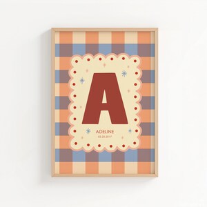 Puede incluir: Una impresi&oacute;n enmarcada con una gran letra "A" de color &oacute;xido sobre un fondo crema festoneado. El fondo es un patr&oacute;n de cuadros en tonos naranja y azul. La impresi&oacute;n incluye el nombre "Adeline" y la fecha "02.20.2017".