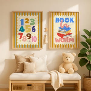 May include: Two framed prints with a yellow and blue striped border. One print displays colorful numbers 1-10. The other print says "BOOK WORM" with a worm on top of stacked books. A beige teddy bear sits on a bench.