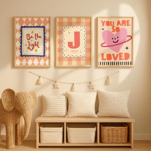 Puede incluir: Tres impresiones art&iacute;sticas enmarcadas con citas inspiradoras y una letra grande. Las impresiones est&aacute;n en un entorno de guarder&iacute;a, con un banco, almohadas y cestas de almacenamiento. El arte presenta una paleta de colores melocot&oacute;n, azul y blanco.