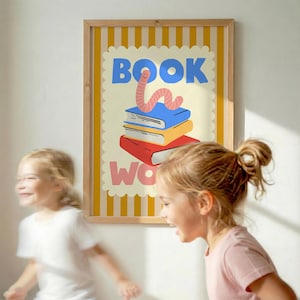 May include: A framed poster with the words "BOOK WORM" in blue and pink, featuring a cartoon worm on a stack of books. The poster has a yellow and white striped background and is in a wooden frame. Two young girls are in the foreground.