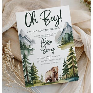 Könnte beinhalten: Babyparty-Einladung mit Aquarellillustrationen von Bergen, Bäumen und einem Bären. Der Text lautet "Oh Bay! Let the Adventure Begin!" und enthält den Namen der Geehrten, Datum, Uhrzeit und Ort.