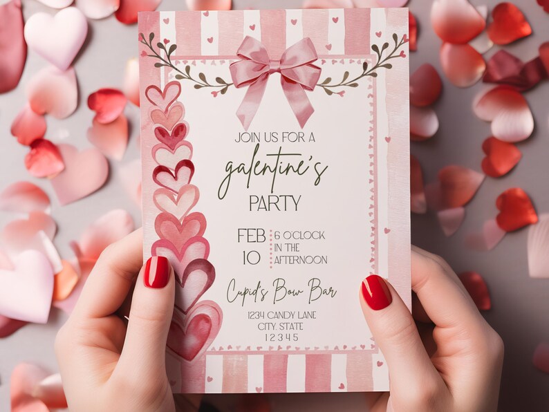 May include: A pink and white Galentine's Party invitation with a bow and heart accents. The invitation includes the text "Join us for a Galentine's Party" and event details. The invitation is held by a person with red nail polish.
