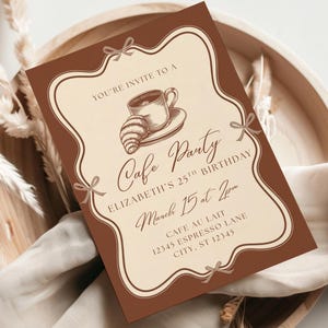 May include: A brown and cream-coloured invitation for a cafe-themed birthday party. The invitation features a coffee cup and croissant illustration, with text that reads "Cafe Party" and event details. The invitation is set on a wooden tray.