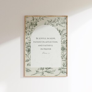 May include: A framed print with a floral design border. The print features a white arch with the text "Be joyful in hope, patient in affliction, and faithful in prayer. Romans 12:12"