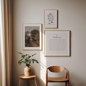 May include: Three framed prints on a light beige wall. The print on the left is a landscape painting of a path through a forest. The print in the middle is a black and white illustration of a flower. The print on the right is a white background with the text "Psalm 23" and the text of the psalm.