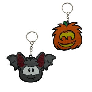 May include: Two keychains featuring cartoon characters. One is a gray bat with red inner ears and white facial markings. The other is an orange pumpkin with a green stem and a yellow face. Both have silver metal rings and chains attached to the top.