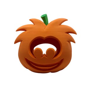 May include: A bright orange pumpkin-shaped decorative object with a smooth matte finish. The pumpkin features a carved-out face with two circular eye openings and a wide, curved mouth opening. A small, solid green stem sits on the top center.