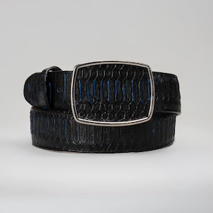 May include: A black leather belt with a silver rectangular buckle. The belt has a textured pattern with blue accents. The buckle has a silver frame and a black center with a similar pattern. The belt is a fashion accessory.