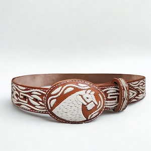 May include: Brown leather belt with a white embroidered horse head design on the oval buckle. The belt features white stitching and a repeating pattern. The belt is a medium width and has a classic design.