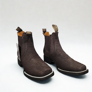 May include: A pair of brown leather ankle boots with a snakeskin texture. The boots have a square toe, a low heel, and a pull tab at the top. The soles are outlined with a silver trim.