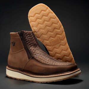 May include: Brown leather ankle boots with a textured snake-skin pattern on the upper and a side zipper. The boots have a white midsole and a tan rubber outsole with a zig-zag tread. A small metal emblem is on the side.