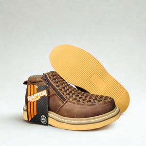 May include: Brown leather Raptor boots with a woven design on the upper and a side zipper. The boots have a thick, tan sole and a matching tag. The sole of the second boot is visible in the background.